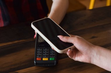 Satın almak için cep telefonu ile ödeme yapan kişinin eli