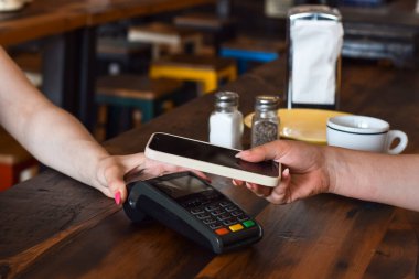 Restoranda veya lokantada cep telefonuyla ödeme yapan kişi, ödeme terminali ve müşterisi olan sunucu elleri
