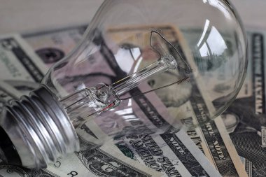 Yanan ampul Amerikan dolarlarının üstüne kağıt para, elektrik maliyeti konsepti