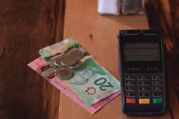 Canadian cash money and payment terminal on restaurant table
