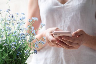 Mavi bahar çiçeklerinin yanında cep telefonu kullanan bir kadının elleri.