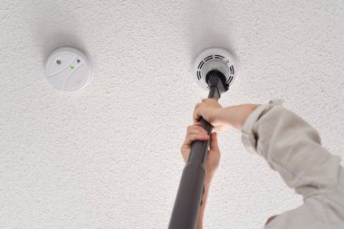 Evcil bir odanın tavanında dumanı ve karbon monoksit detektörlerini temizleyen bir kadın.