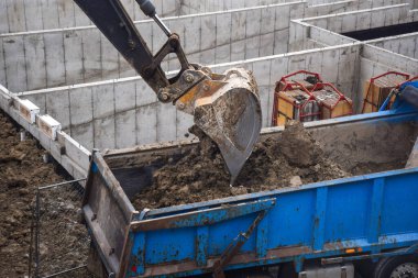 Kazıcı inşaat alanındaki çöp kamyonuna toprak yükleyip çıkarıyor.