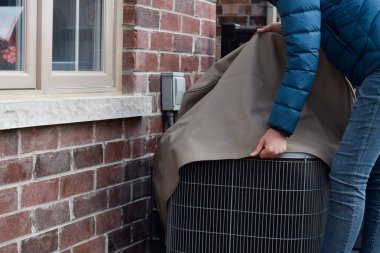 Woman putting cover on air conditioner unit outside the house clipart