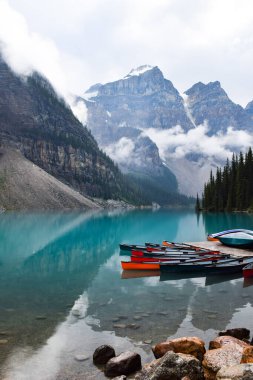 Banff Alberta 'da dağlarla çevrili mavi Moraine gölüne dizilmiş renkli bir kano.