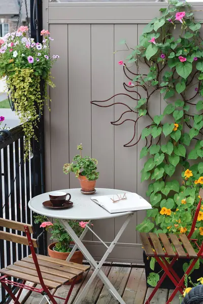 Bistro seti, kitap ve kahve fincanı bitkilerle çevrili bir apartman balkonunda.