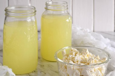 Yeni yapılmış süzme peynir ve mutfak tezgahındaki cam kavanozlarda kalan sıvı süt.