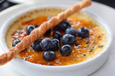 Creme brulee, taze yaban mersiniyle süslenmiş bir restoranda beyaz bir tabakta tatlı.