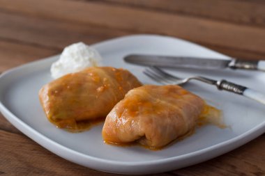 Geleneksel Ukrayna lahanası beyaz bir tabakta ekşi kremayla yuvarlanıyor.