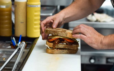 Restoran çalışanı müşteri siparişi için kulüp sandviçi hazırlıyor.
