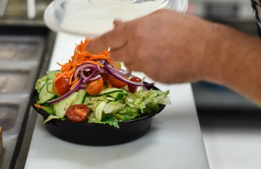 Restoran çalışanı sipariş için plastik konteynırda salata paketliyor.
