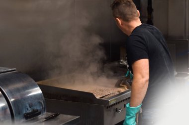 Adam restoranın mutfağında ızgara temizliyor.