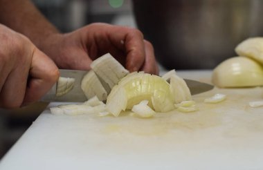 Restoran çalışanı, soğanları yakın plan bıçakla kesiyor.