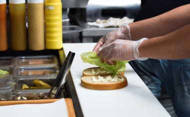 Mutfak çalışanı, yemek siparişi için sandviç hazırlıyor.