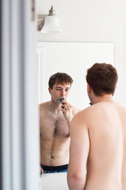 Genç adam banyoda Mirrow 'un önünde tıraş oluyor.
