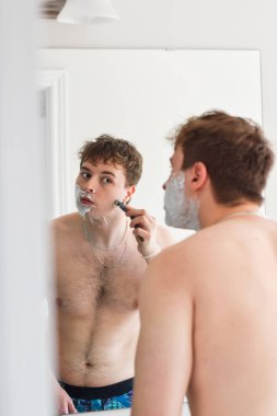 Genç adam banyoda Mirrow 'un önünde tıraş oluyor.
