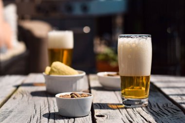 Bahçe masasında iki bira bardağı, cips ve fıstık.