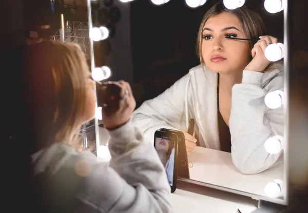 Genç bir kız sosyal medya için ışıklandırmalı aynanın önünde bir video kaydederken rimel sürüyor. 