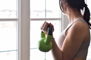 Evde pencerenin önünde çalışırken biseps olarak ağırlık kullanan genç bir kız.