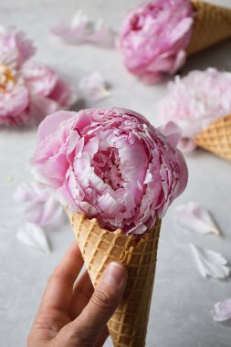 Pembe şakayık çiçekli waffle dondurma külahını tutan bir kadın eli.