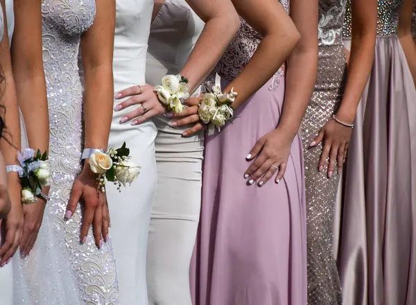 Resmi balo elbiseli ve çiçek desenli bir grup genç kadın fotoğraf için birbirlerine poz veriyorlar.