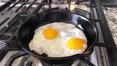 İki güneşli tarafı gaz ocağında demir bir tavada kızaran yumurtalar.