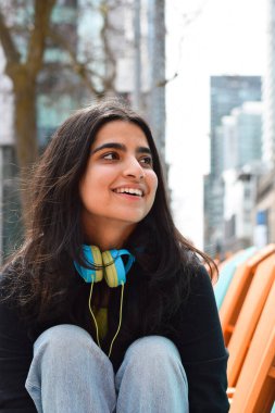 Şehir caddesinde oturmuş gülümseyen mutlu genç kızın yakın plan portresi.