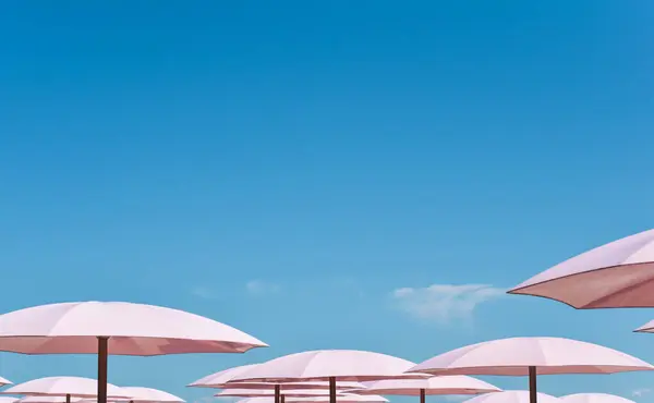 Mavi gökyüzüne karşı en az pembe plaj şemsiyesi görüntüsü.