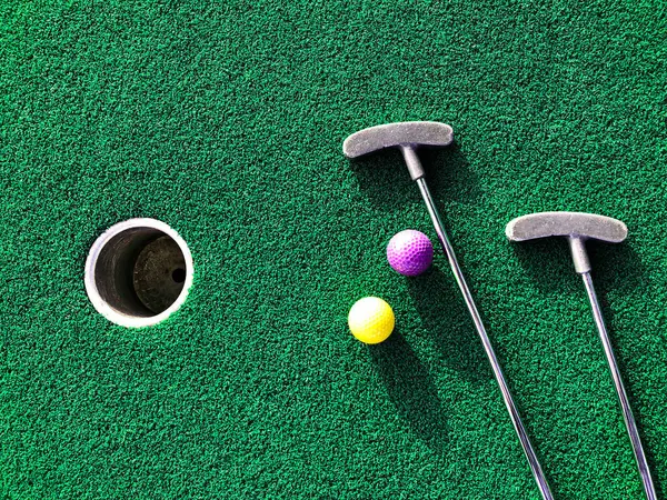 Yeşil arka planda mini golf sopaları ve topları 