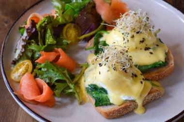 Benedict usulü yumurta, füme somon ve taze yeşil salata ile yakın kahvaltı tabağı.