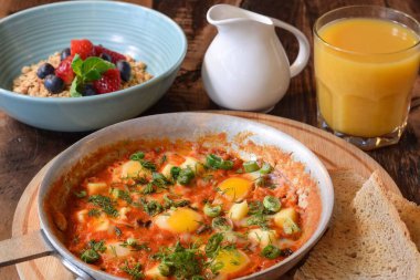 Kahvaltı Shakshuka ve bir kase tahıl gevreği ile ahşap masada portakal suyu.