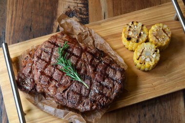 Tahtada ızgara biftek ve ızgara mısırla biberiye filizi servis edilir.