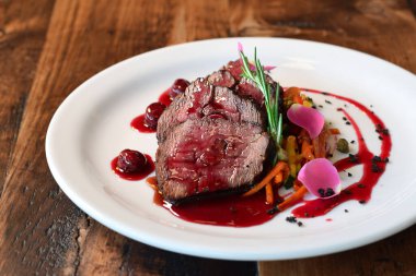 Dilimlenmiş dana eti, jülyen sebze ve kiraz sosuyla servis edilir. Biberiye filizi ile süslenir.