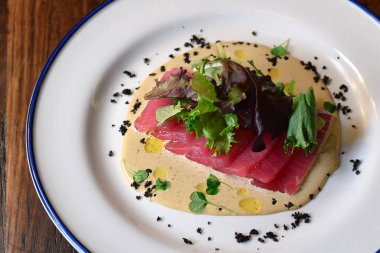 Karışık marul yeşiliyle süslenmiş ton balığı carpaccio tabağı.