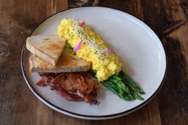 Çırpılmış yumurta, pastırma, buğulanmış kuşkonmaz ve ahşap masada kızarmış ekmek.