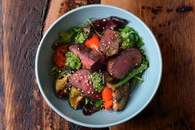 Sıcak dilimlenmiş biftek ve ahşap masada ızgara sebze salatası.