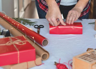 Kadının elleri Noel hediyelerini kırmızı kağıda sarmak için bant kullanıyor.