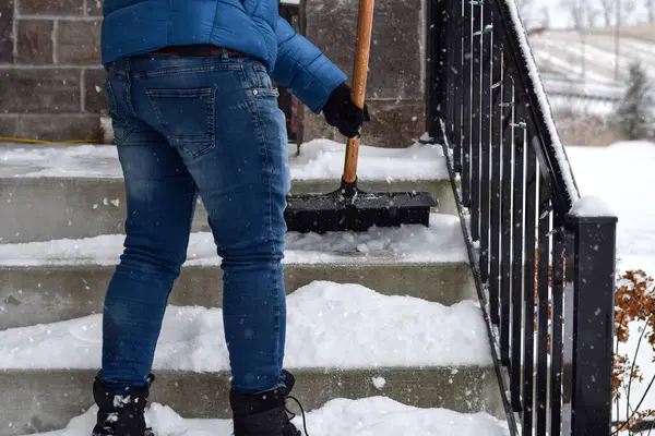 Kar yağarken evin ön merdivenlerinden kar temizleyen bir adam.