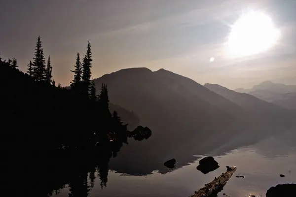Britanya Kolumbiyası 'ndaki Garibaldi Gölü' nün üzerinde batan güneş sakin sularda altın bir parıltı yayıyor. Yükselen dağ siluetleri ve sonsuza dek yeşil yansımalar, alacakaranlıktaki Kanada alp ormanlarının güzelliğini vurgulayan sakin ve dramatik bir sahne yaratır..