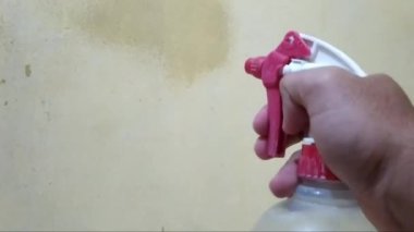 Sarı arka planda elinde sprey şişesi olan bir adamın sarı duvarına doğru su püskürtüyor..