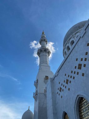 Şeyh Zayed Büyük Camii 'nin güzel bir şekilde inşa edilmiş beyaz minaresi bulutlu mavi gökyüzünün altında dimdik ayakta duruyor. Karmaşık mimari özellikler ve İslami kültür mirası gösterimi. 
