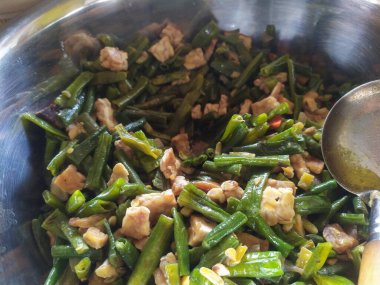 Görüntü, kabın içindeki uzun fasulye ve tempeh 'in sebze menüsünü gösteriyor..