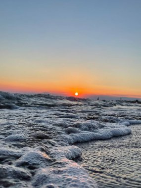 Ufuk mavisi gökyüzü ve deniz köpüklü küçük dalgalar ile denizde turuncu gün batımı kameraya yakalandı. Yüksek kalite fotoğraf. Seyahat fotoğrafı..