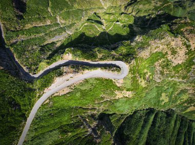 Portekiz 'deki Madeira adasında, verimli yeşil ormanlar ve dik yamaçlarla çevrili dolambaçlı bir dağ yolunu gözler önüne seren çarpıcı bir insansız hava aracı görüntüsü, doğanın güzelliğini ve uzak manzaralardaki mühendisliğin mucizesini vurguluyor.