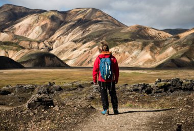 Canlı bir dağda, renkli tepeler ve dramatik manzaralarla çevrili Landmannalaugar 'ı tek başına ayakta tutan yürüyüşçü. Sahne macera, yalnızlık ve el değmemiş vahşi doğayla bağlantı hissi uyandırıyor.