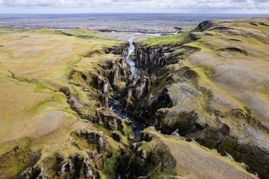 A stunning aerial drone perspective a peaceful river cutting through Grand Fjadrargljufur Canyon in Iceland surrounded by luscious green and rocky cliffs, evoking awe and admiration natural landscapes clipart