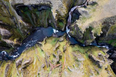 Göz kamaştırıcı bir hava aracı perspektifi İzlanda 'daki Büyük Fjadrargljufur Kanyonu' ndan geçen huzurlu bir nehir etrafını çevreleyen yeşil ve kayalık uçurumlar, hayranlık ve hayranlık uyandıran doğal manzaralar.
