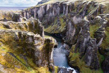 A stunning aerial drone perspective a peaceful river cutting through Grand Fjadrargljufur Canyon in Iceland surrounded by luscious green and rocky cliffs, evoking awe and admiration natural landscapes clipart