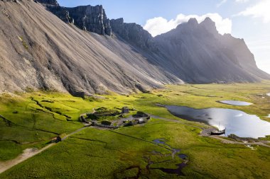 İzlanda 'nın Stoksnes kentindeki Vestrahorn dağlarıyla çevrili bir Viking köyü yeşil bir vadinin havadan görüntüsü. Gölleri ve tarihi yapıları olan sakin bir atmosfer.