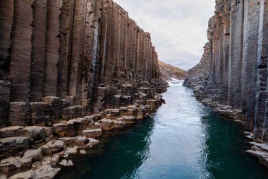 Havadan manzaralı büyüleyici bir bazalt Studlagil Kanyonu turkuvaz nehrinin akışıyla doğal olarak oluşmuş, çarpıcı sütun kaya oluşumlarını vurguluyor, Haziran ayında İzlanda yakınlarındaki yeşillik